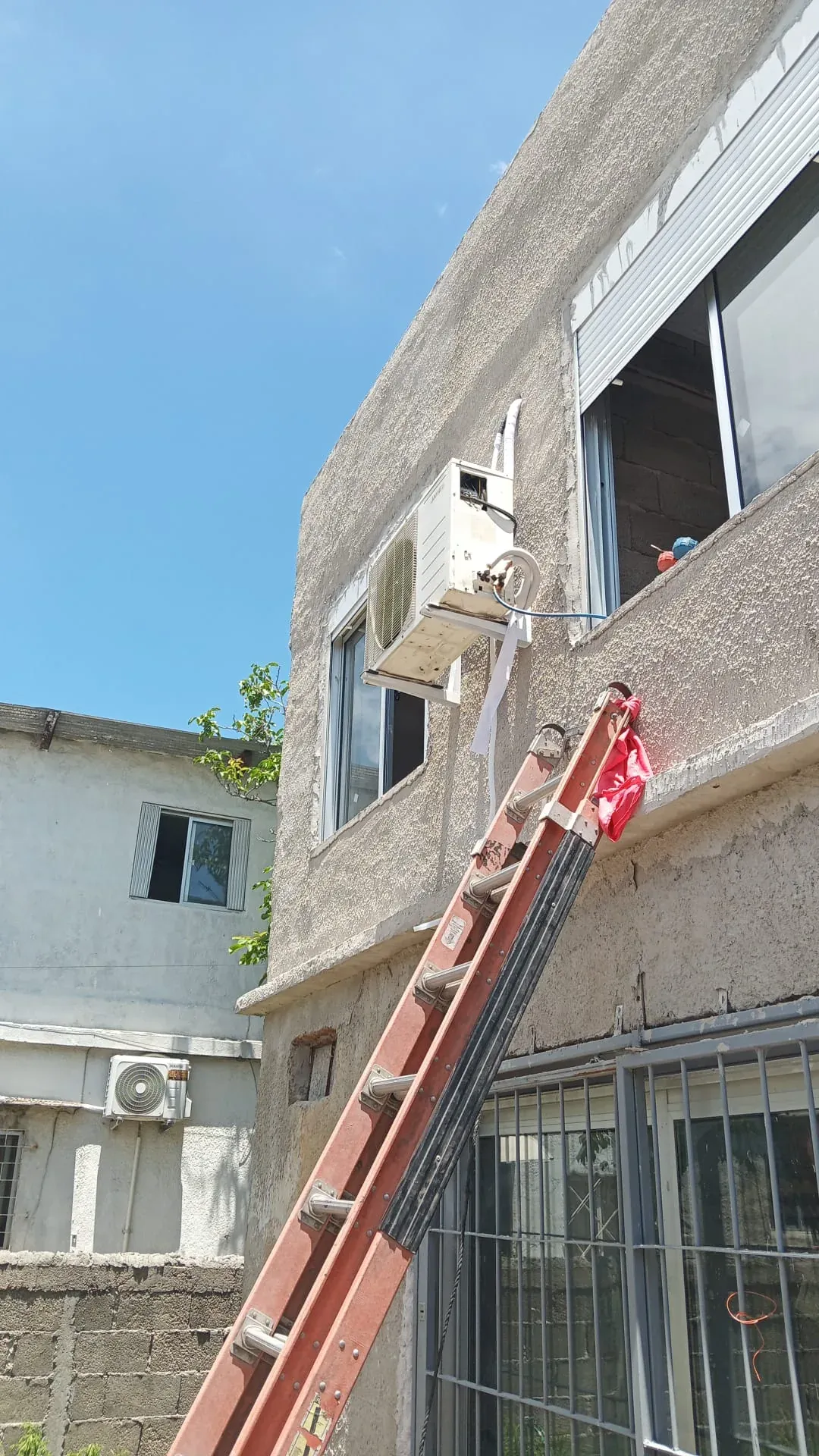 Desmontaje en altura de una unidad exterior de aire acondicionado, con escalera apoyada en la fachada