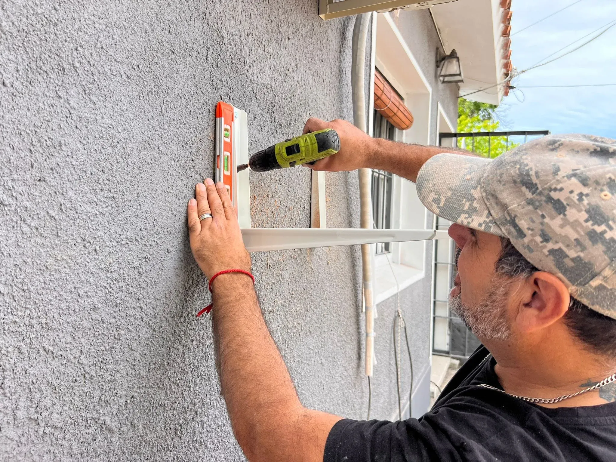 Técnico de 100% AIRE fijando con nivel y taladro el soporte de la unidad exterior de un aire acondicionado en la pared de una casa
