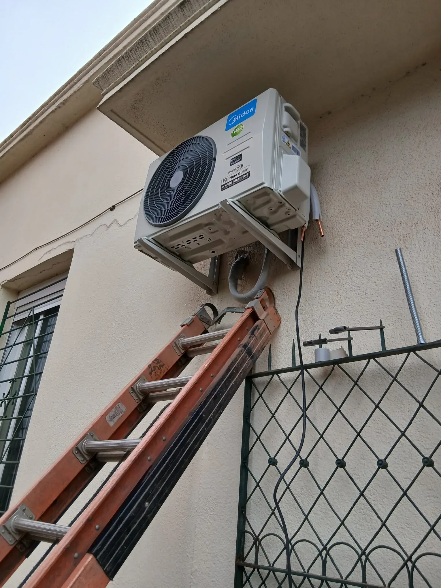 Unidad exterior de aire acondicionado Midea Inverter instalada sobre soportes metálicos en la fachada de una casa